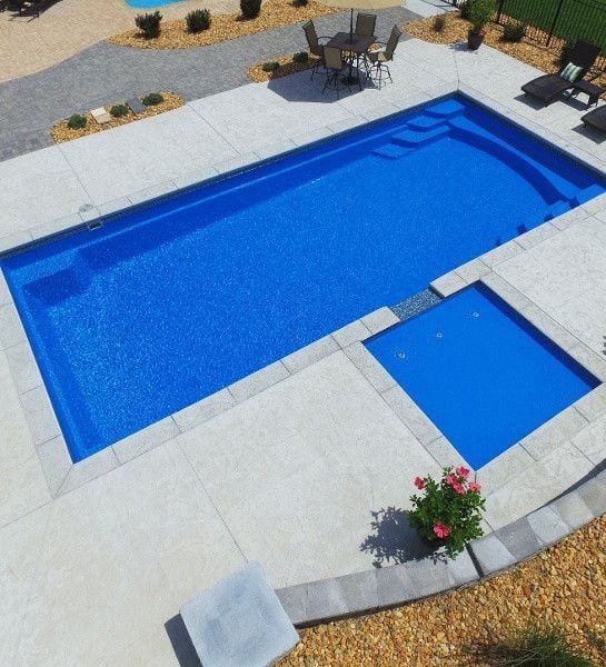 Blue swimming pool with attached spa in a landscaped backyard patio