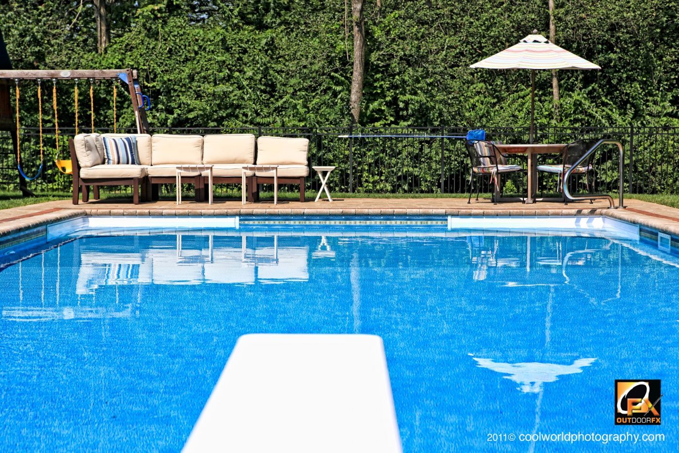Backyard swimming pool with lounge chairs, umbrella, and patio furniture beside a hedge.