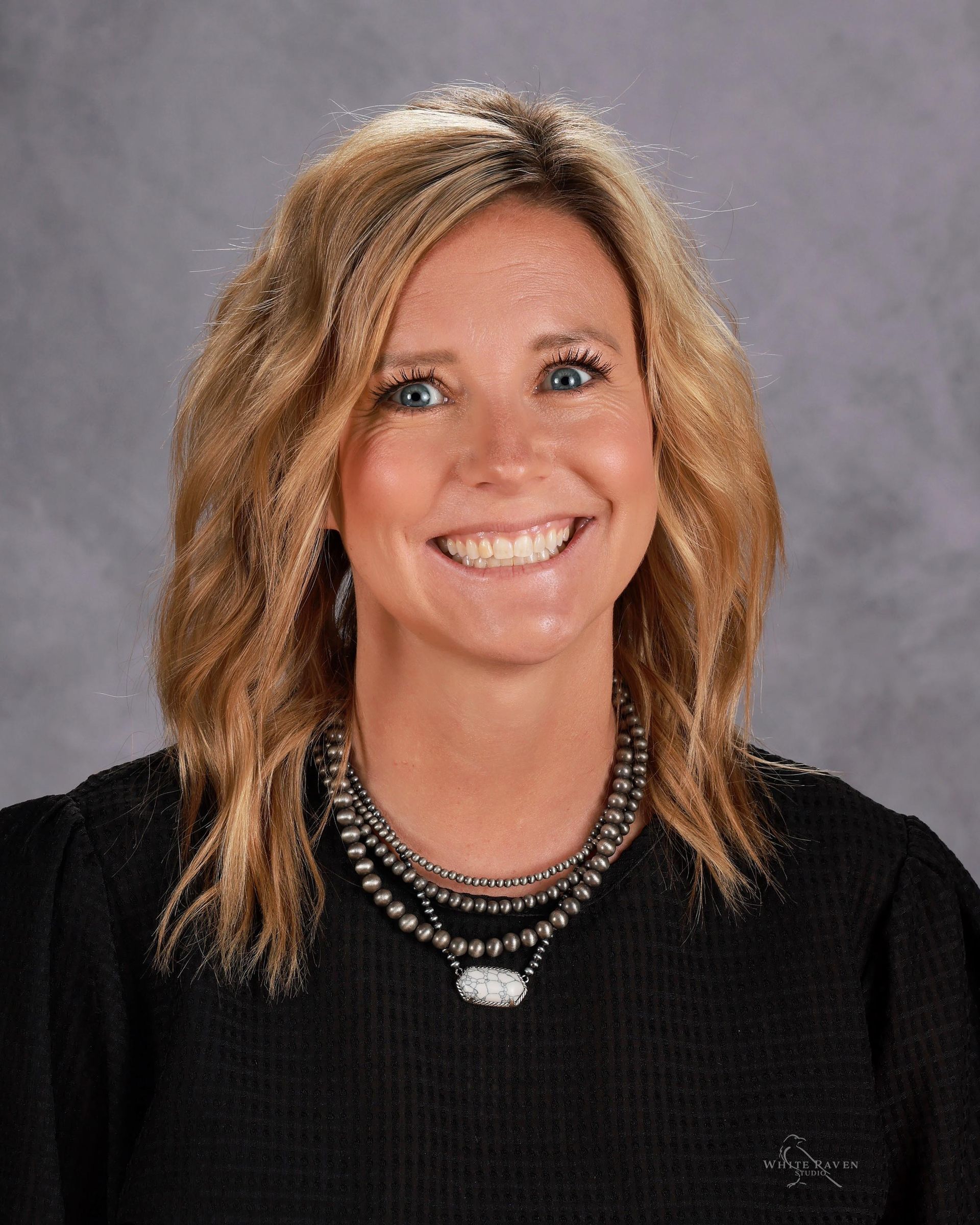 A woman with blonde hair and blue eyes is smiling for the camera.