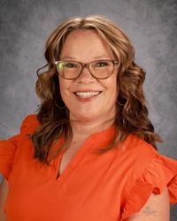 A woman wearing glasses and a blue shirt is smiling for the camera.