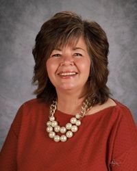 A woman wearing a pearl necklace and earrings is smiling for the camera.