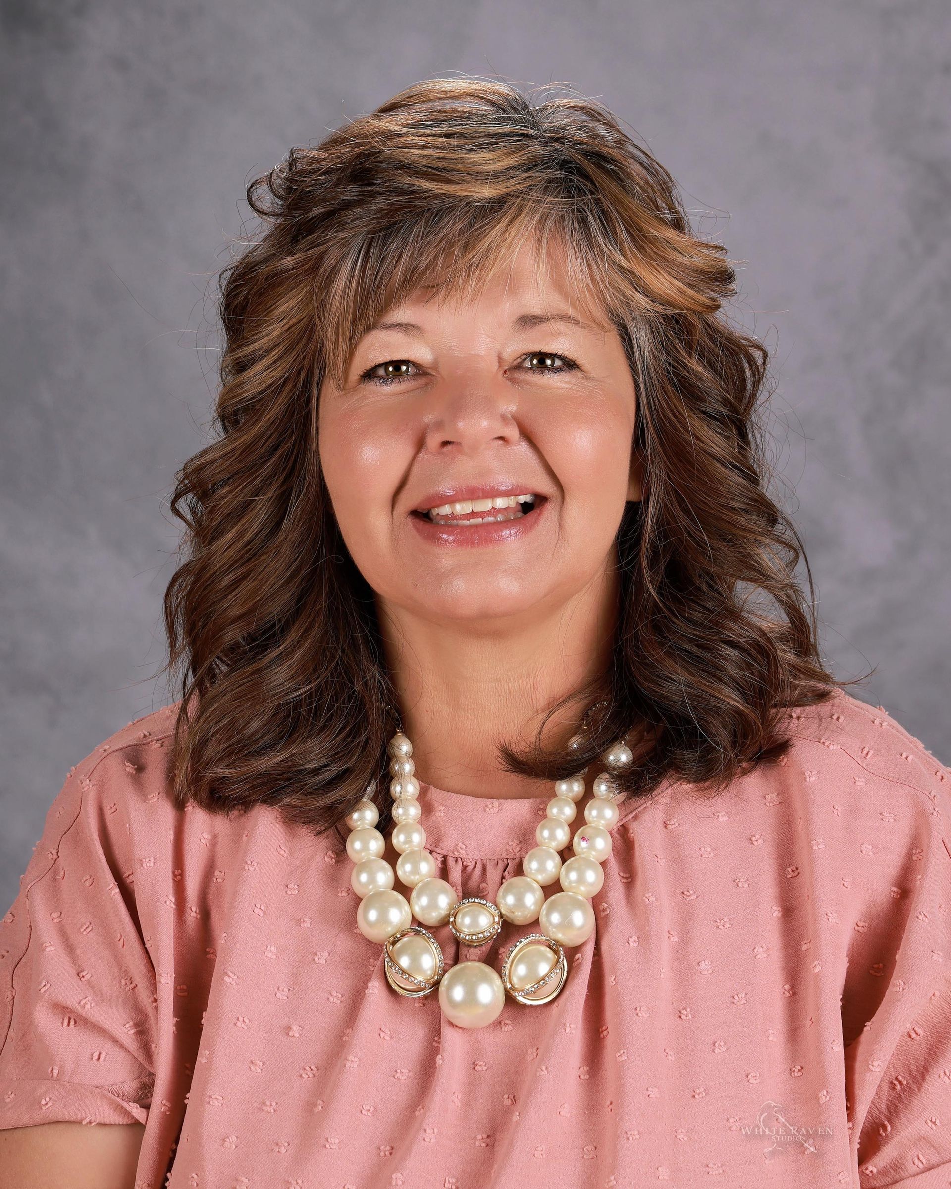 A woman wearing a pearl necklace and earrings is smiling for the camera.