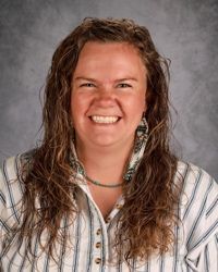 A woman with curly hair is smiling and wearing a necklace.