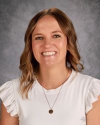 A woman wearing a white shirt and a necklace is smiling for the camera.