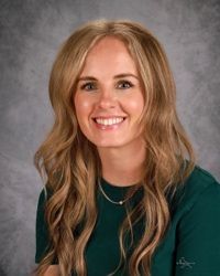 A woman with blonde hair and a necklace is smiling for the camera.
