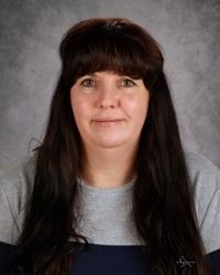 A woman with long brown hair and bangs is smiling for the camera.