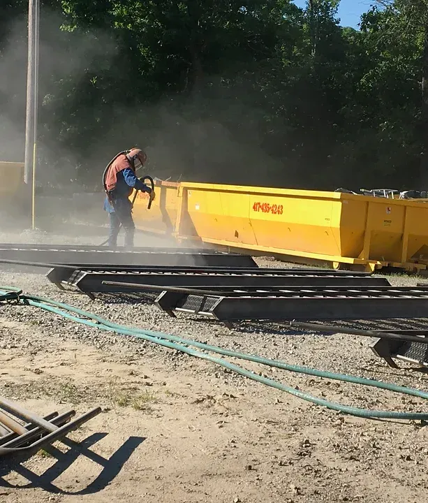 a man is sandblasting a yellow dumpster in the dirt
