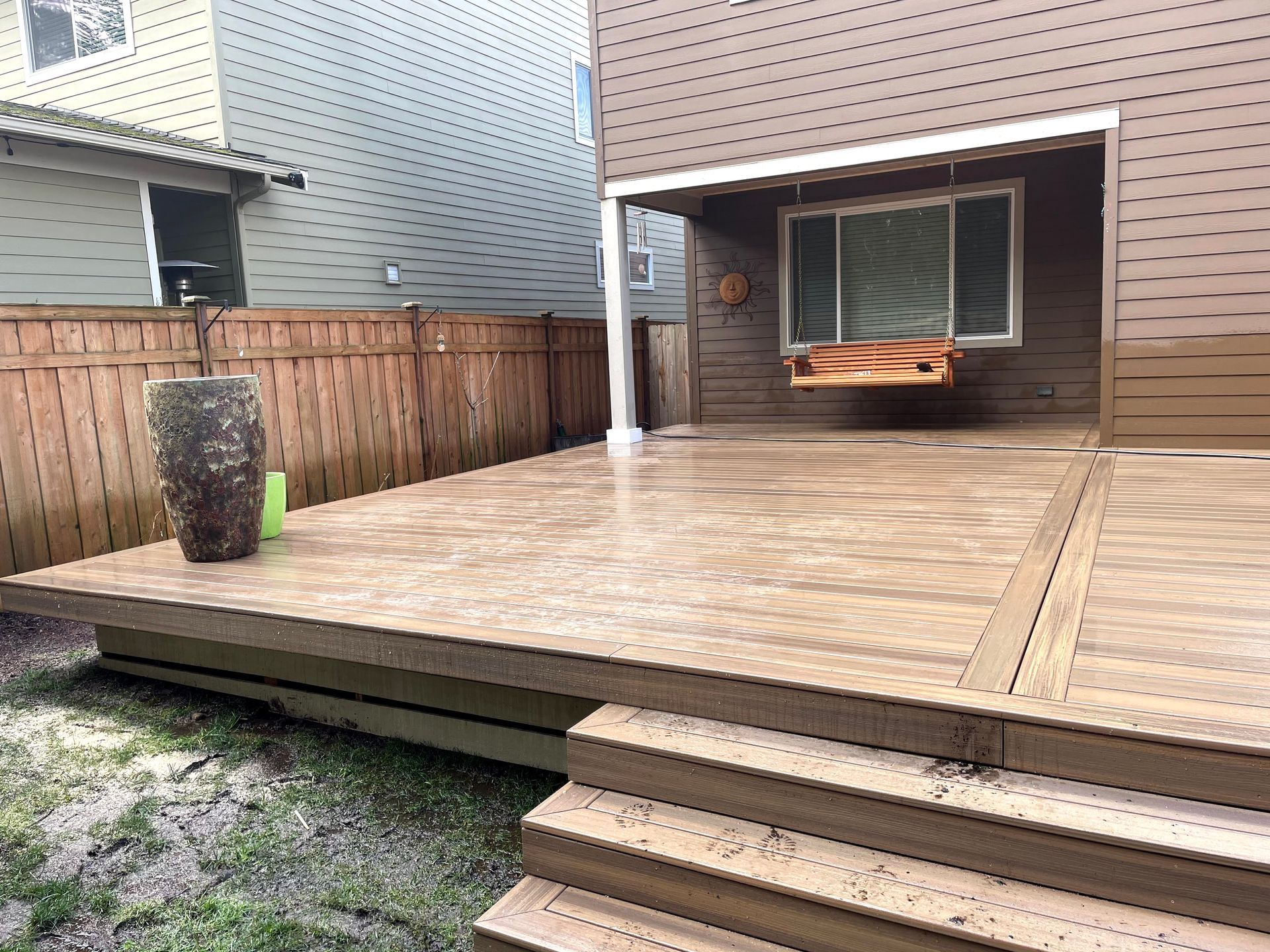 Wooden backyard deck with steps, fenced yard, and a covered patio holding an orange couch.