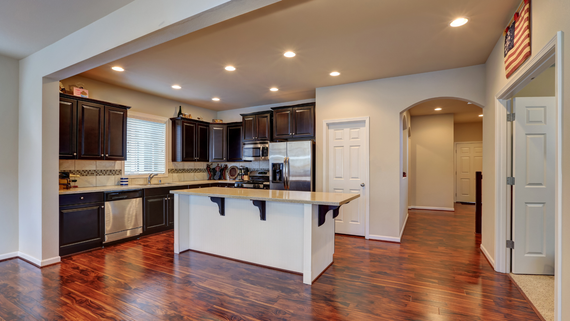 A kitchen featuring dark wood cabinets, a white center island with stools, stainless appliances, and hardwood flooring.