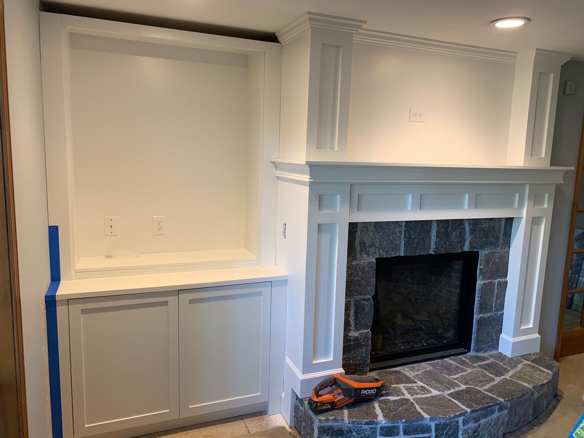 Built-in white fireplace with gray tile hearth beside a white cabinet and window seat.