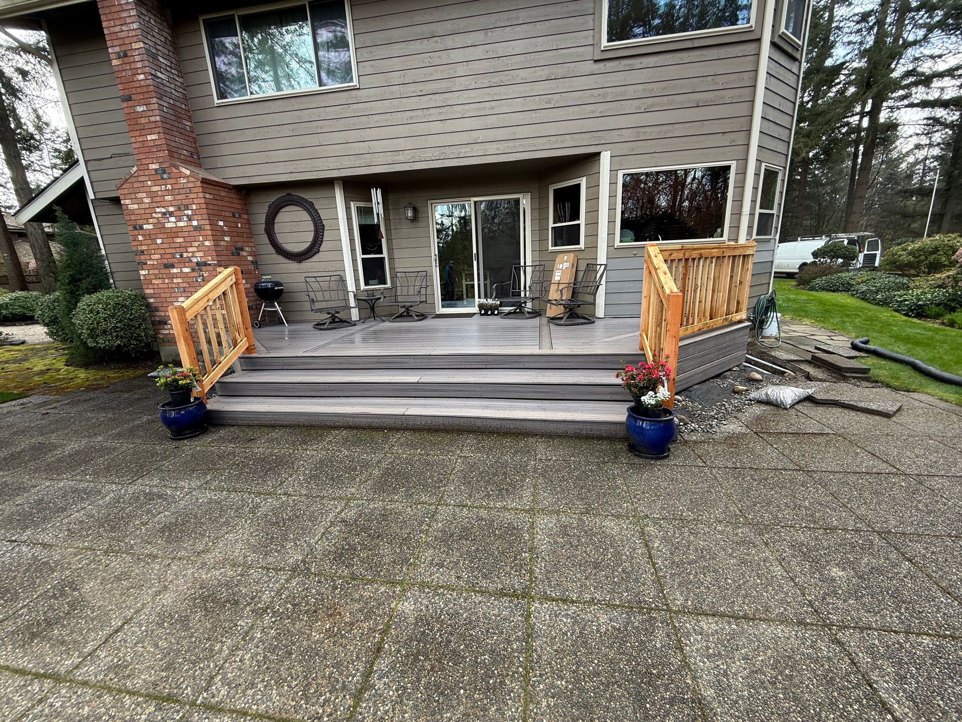 Front view of a house entry with a wide concrete driveway, steps, and wooden railings with potted flowers.