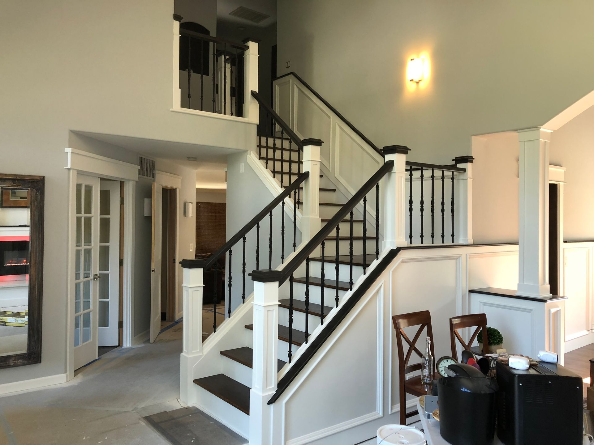 Bright foyer with a staircase, white walls, black railings, and French doors in a two-story home