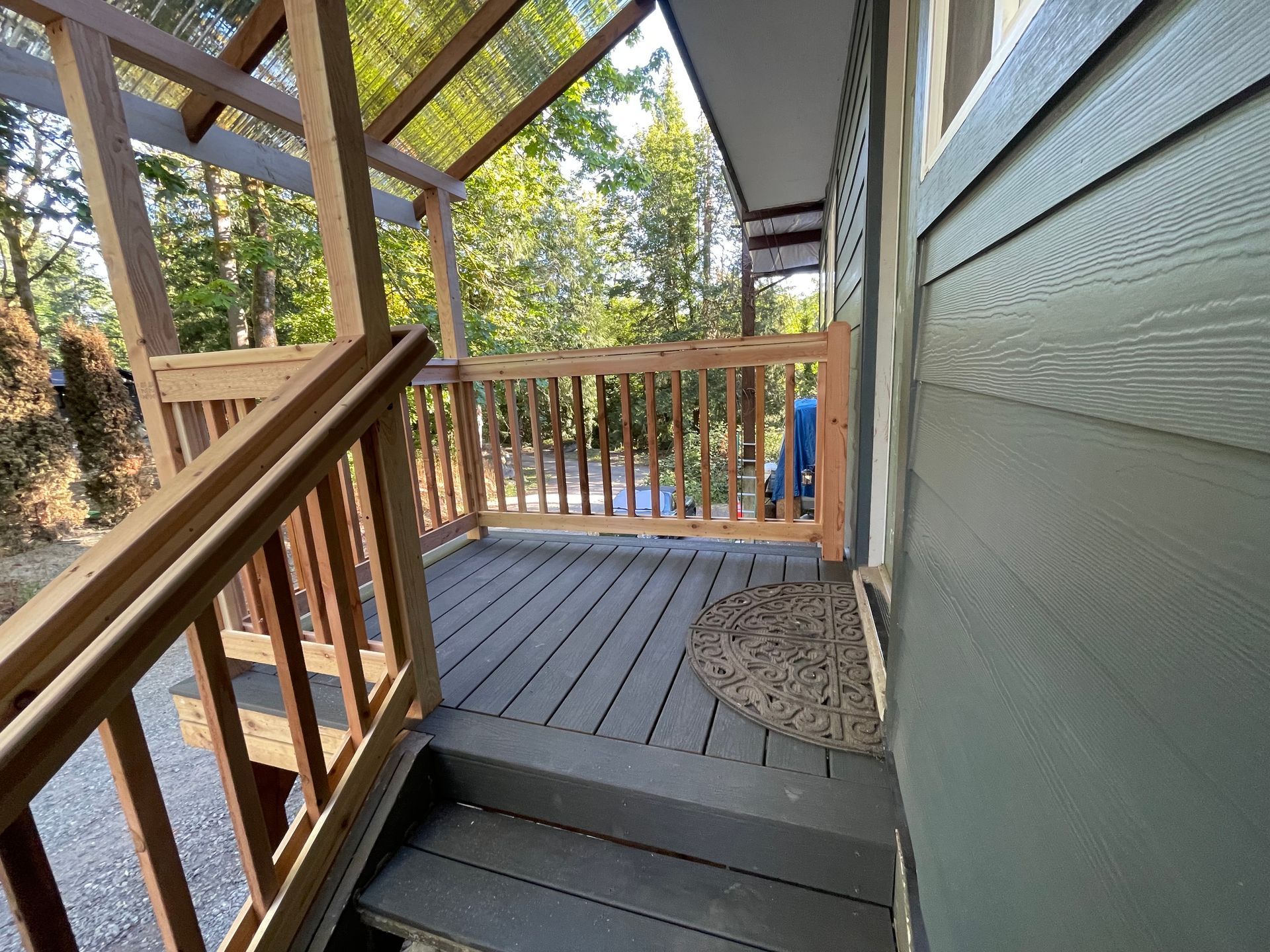 Wooden porch and deck walkway with railings beside a house, leading to an outdoor yard.