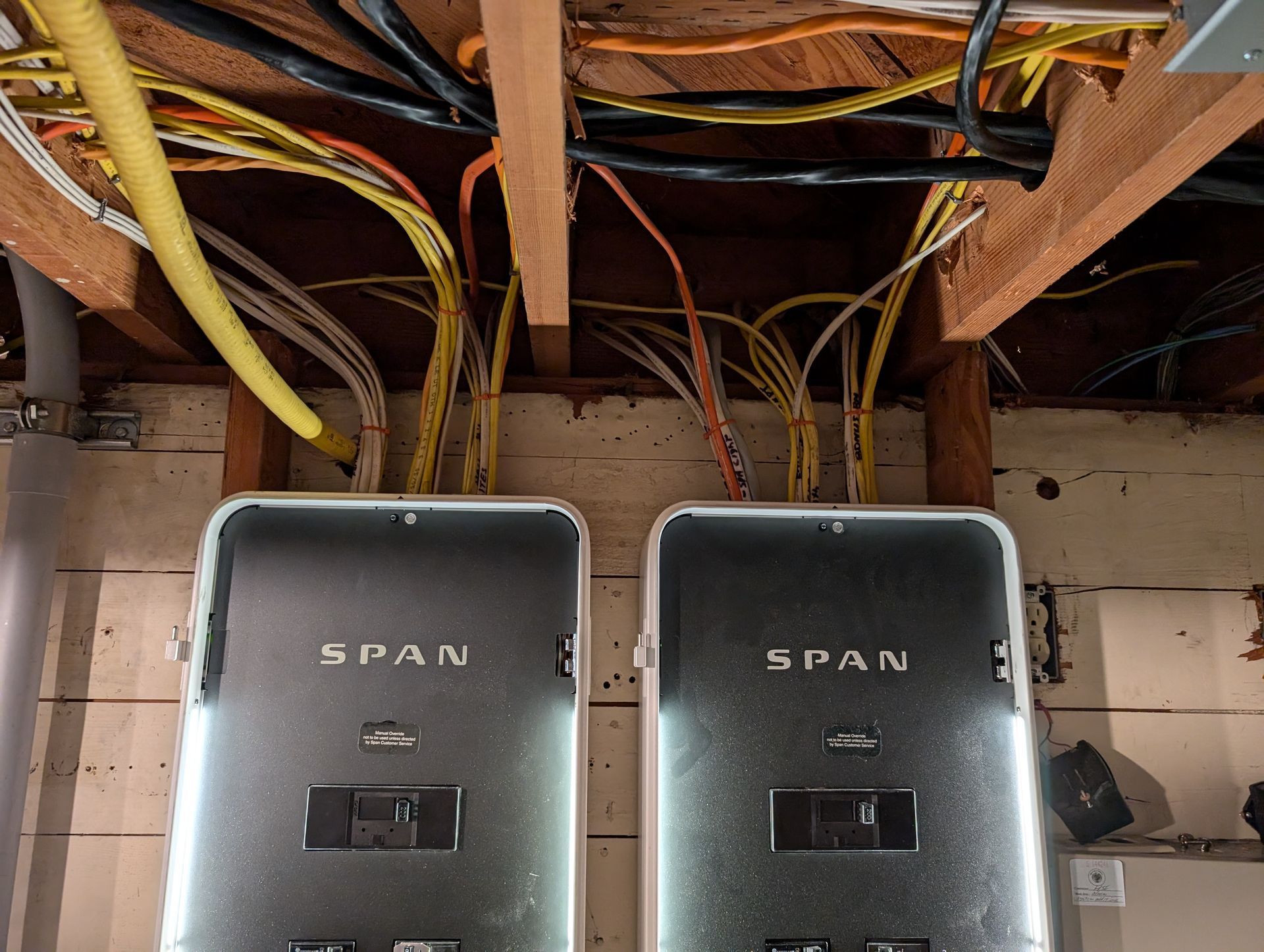 Two gray SPAN electrical panels beneath exposed wiring in a utility room