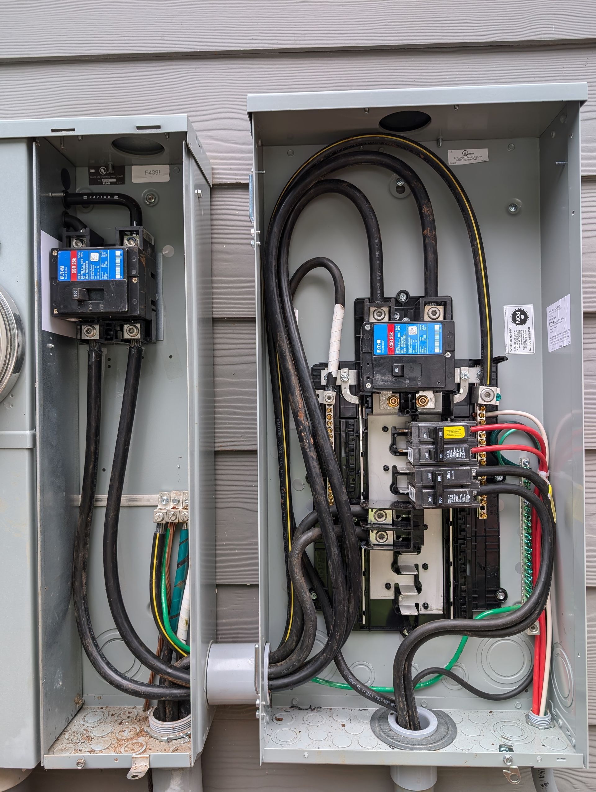 Two open electrical service panels with exposed wiring and breakers on a wall