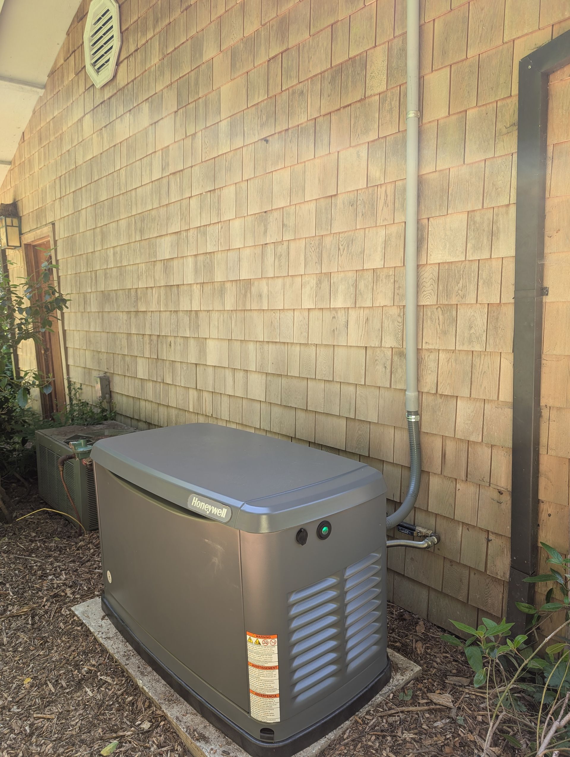 Outdoor metal generator beside a tan shingle wall on gravel