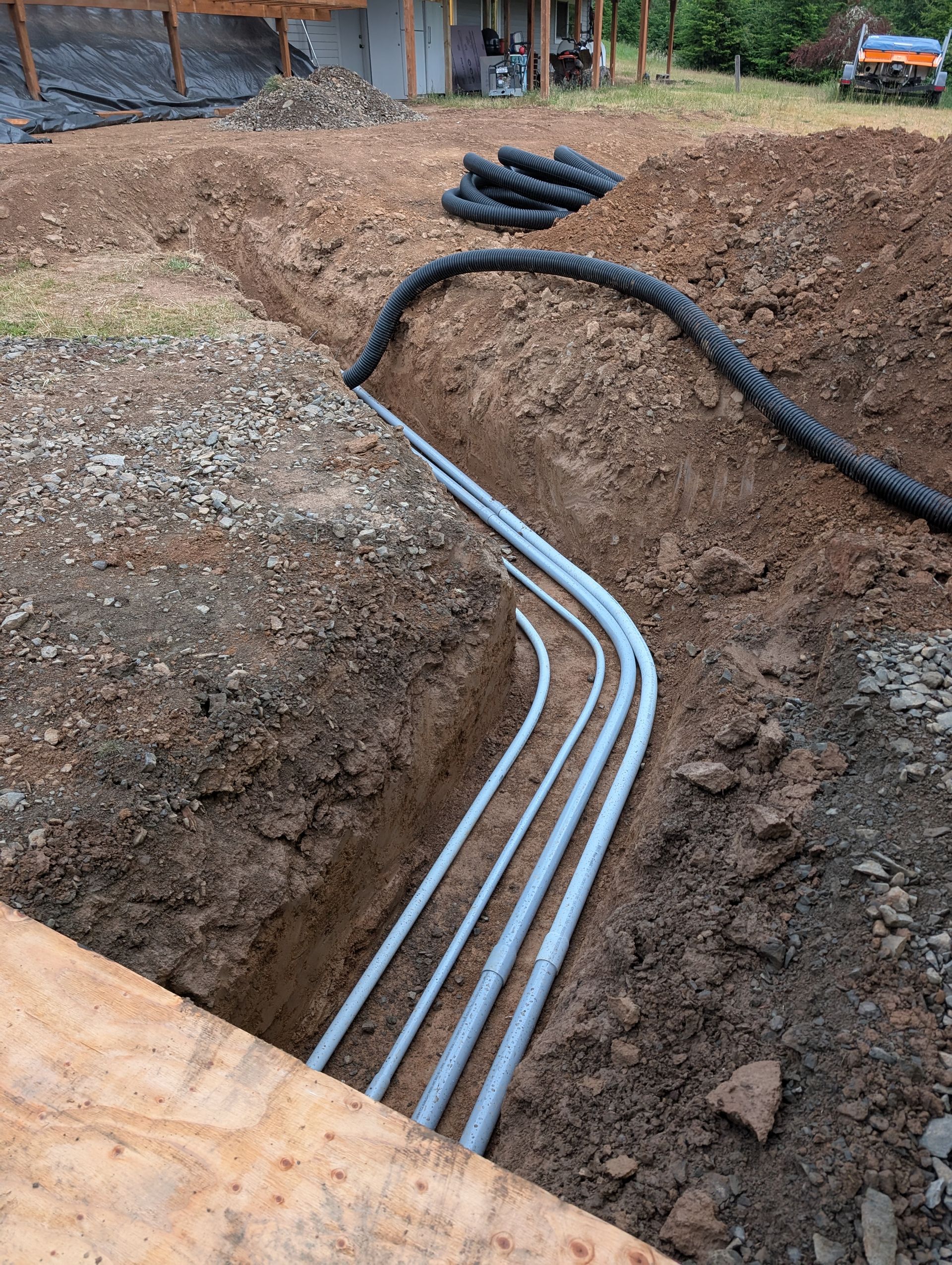 Open trench with four gray utility conduits laid in dirt at a construction site.