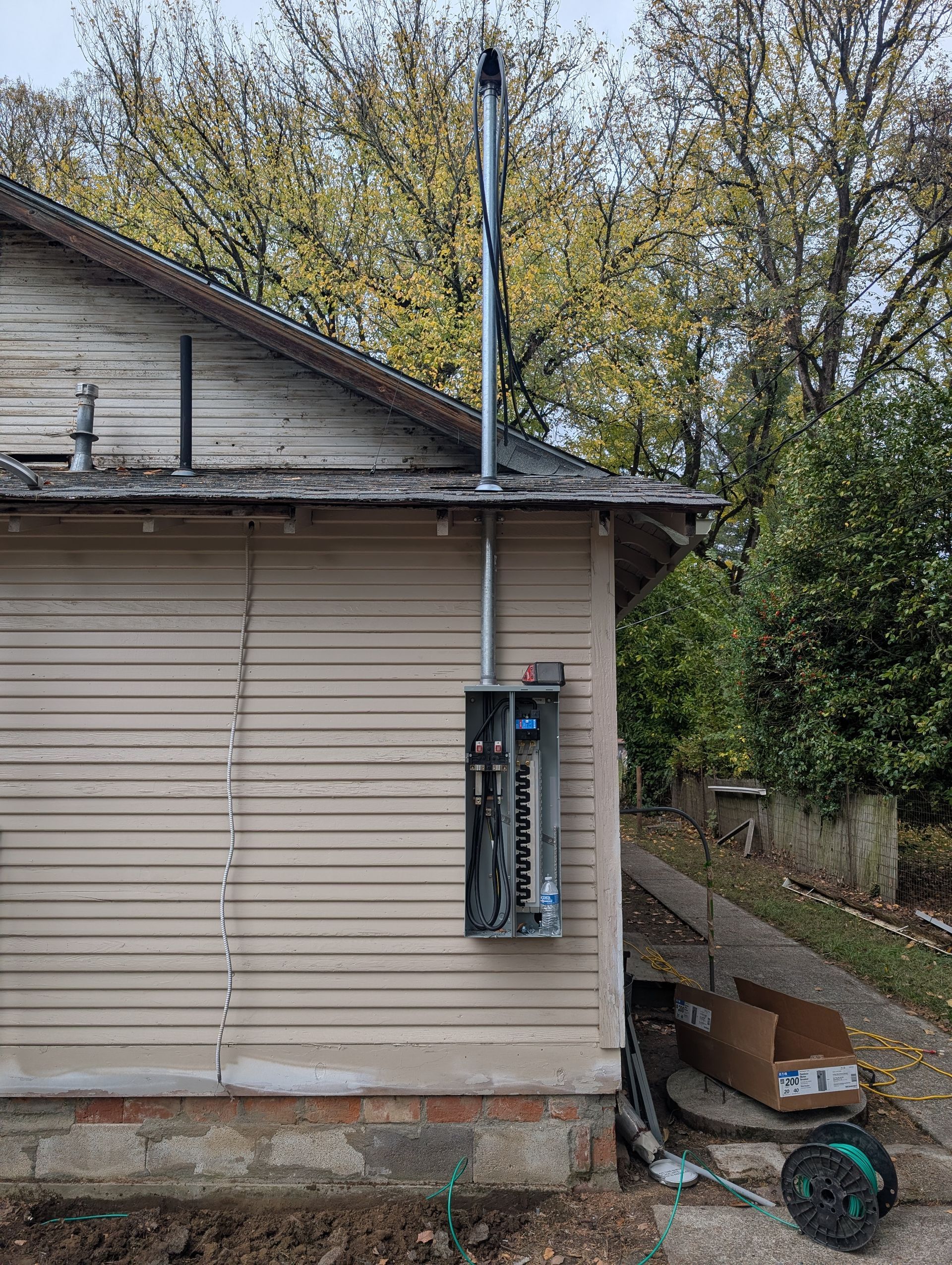 Exterior side of a house with an electrical panel, utility pole, and overgrown yard clutter.