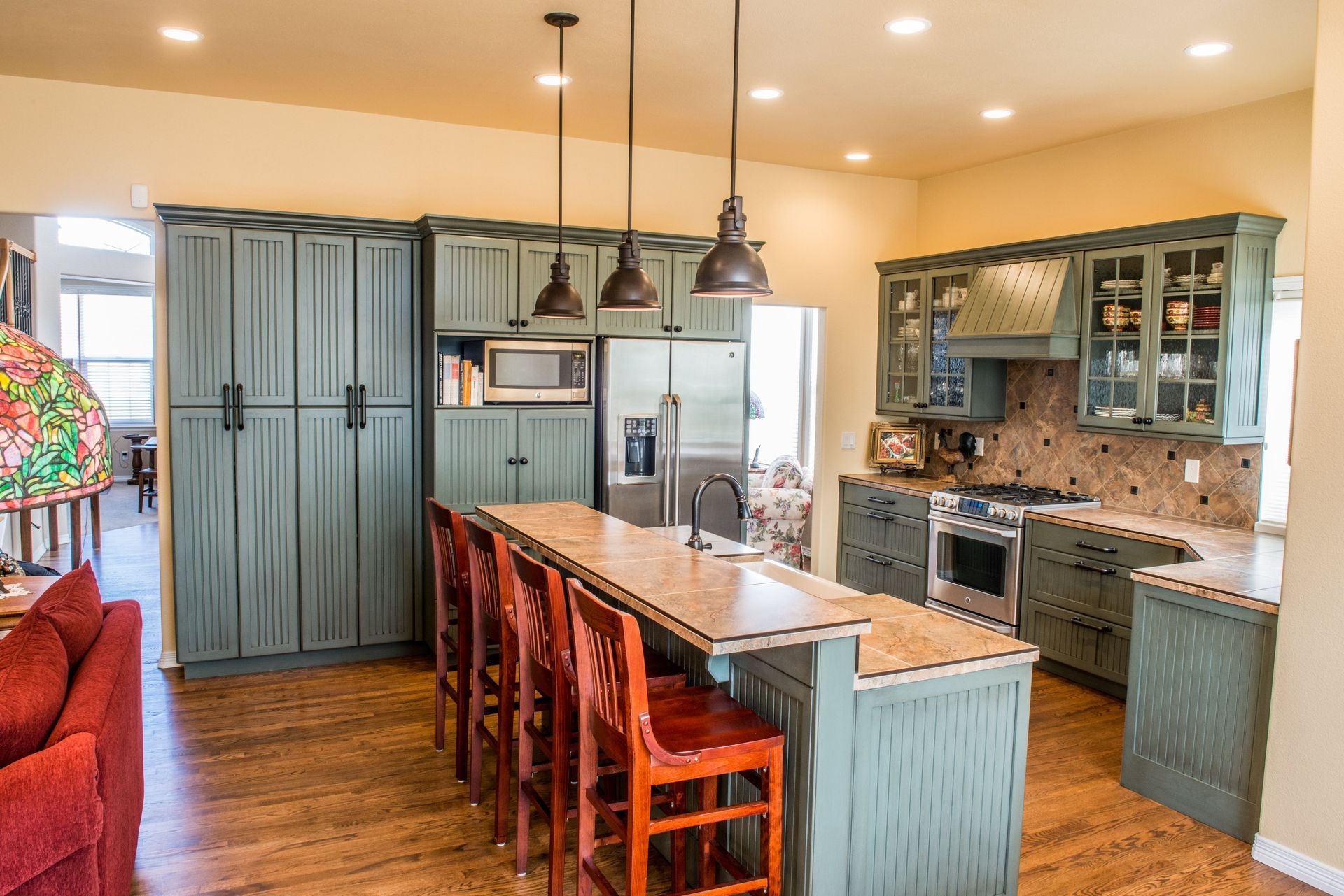 A kitchen with sage green cabinets, a wood-topped island with stools, stainless steel appliances, and wood flooring.