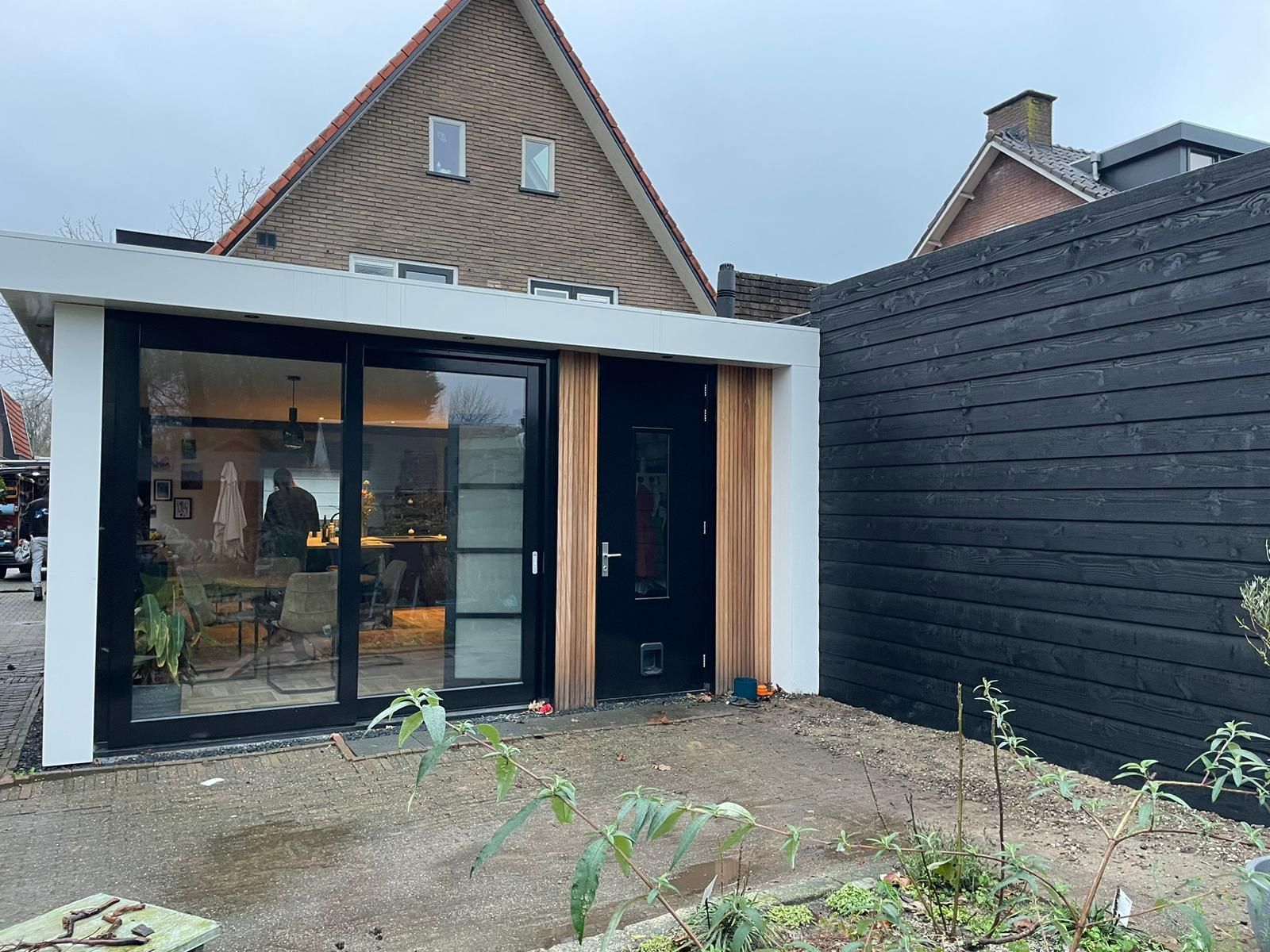 Gerenoveerde moderne witte aanbouw donkere ramen. Uitbouw tuinkamer verbouwing.