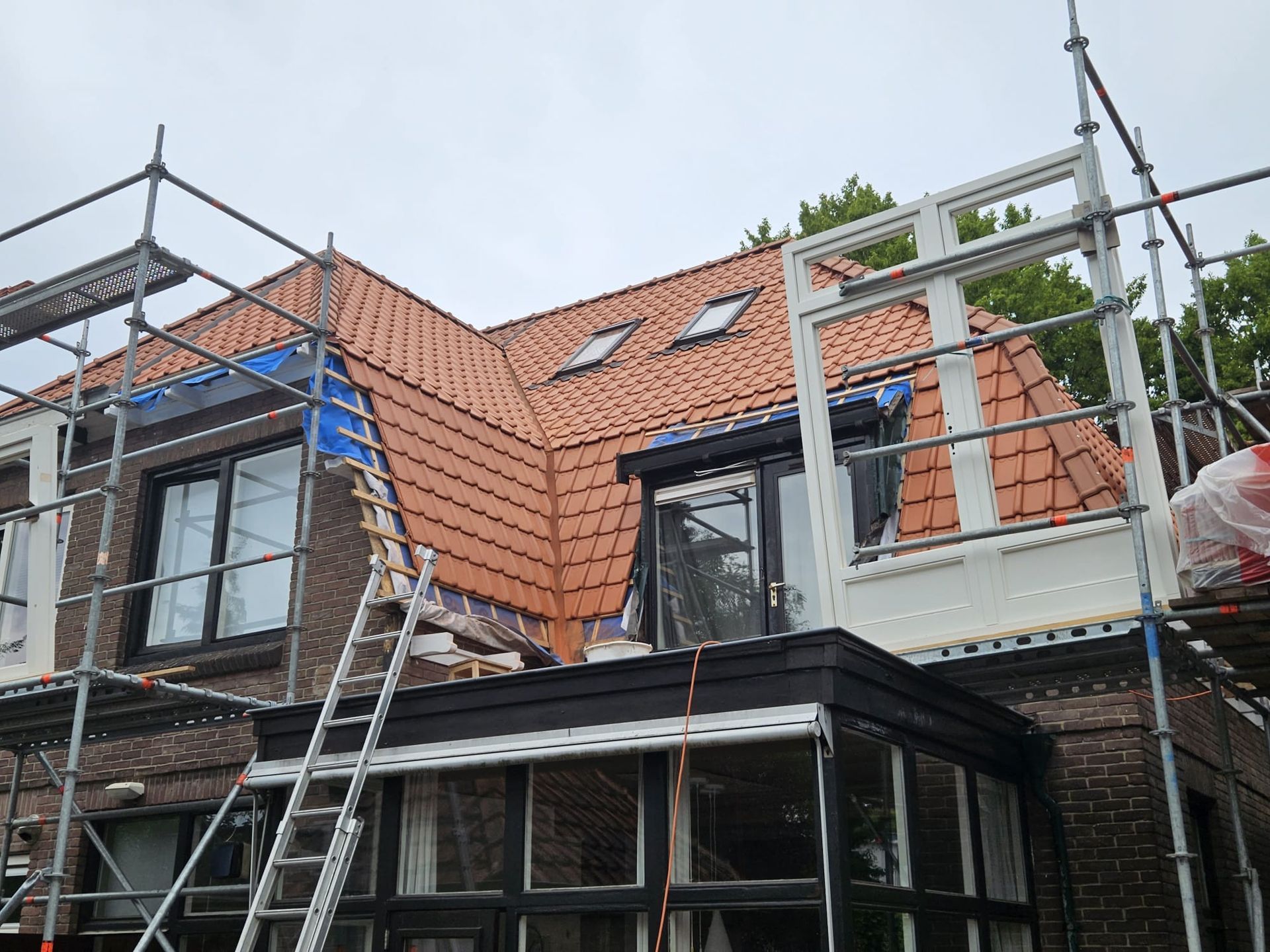 Dakwerk in aanbouw met steiger. Rode dakpannen installatie. Aannemer werkzaamheden zichtbaar.