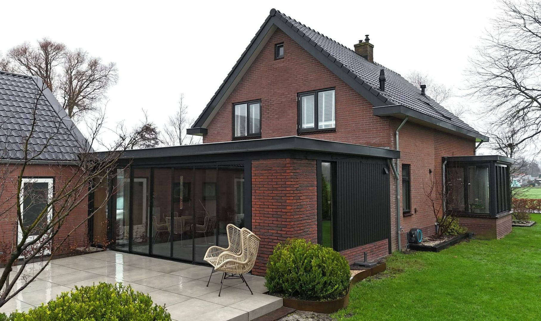 Gerenoveerd baksteenhuis met donkergrijze uitbouw. Aannemer renovatie woning met grote ramen.