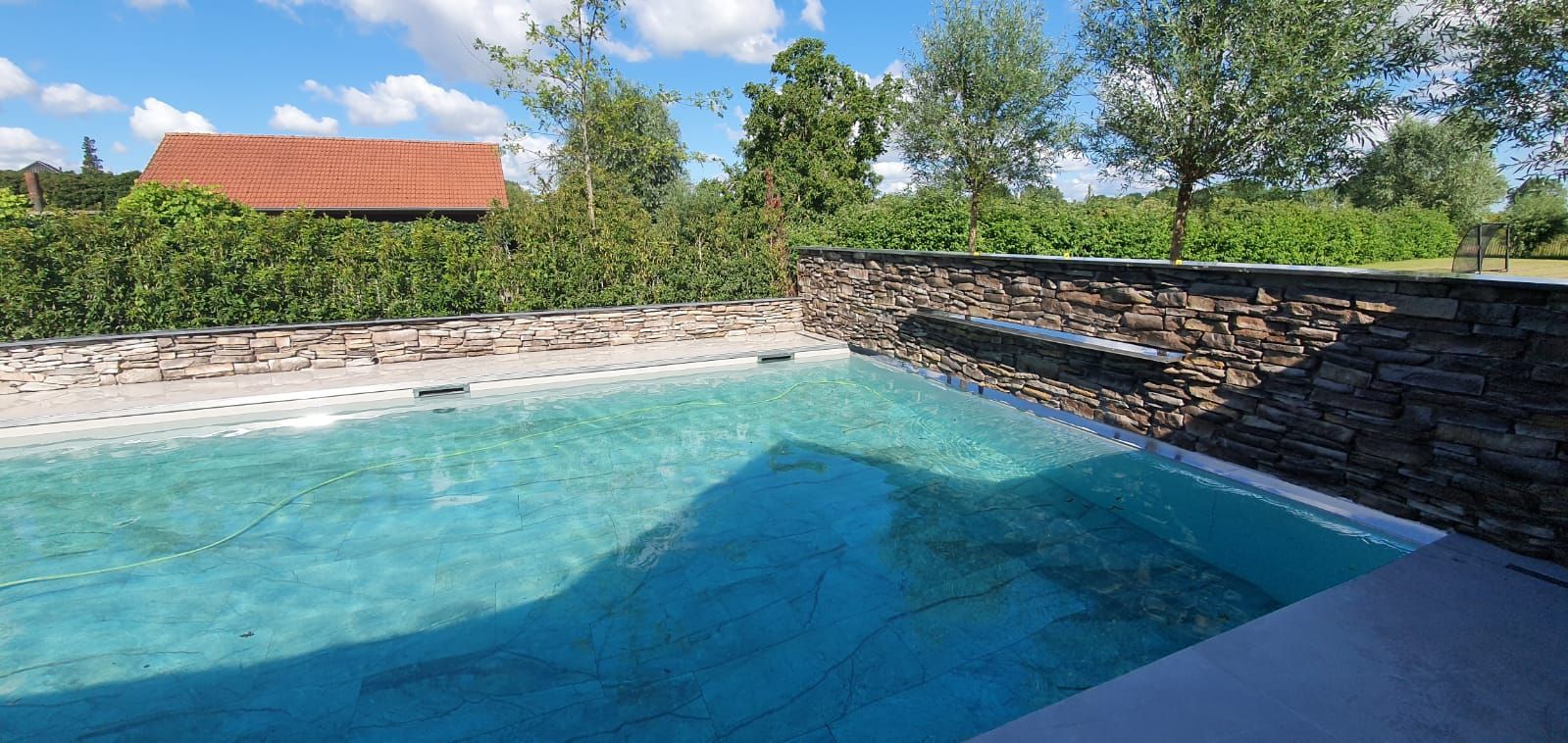 Zwembad gerenoveerd stenen omheining. Tuinverbouwing waterpalen design