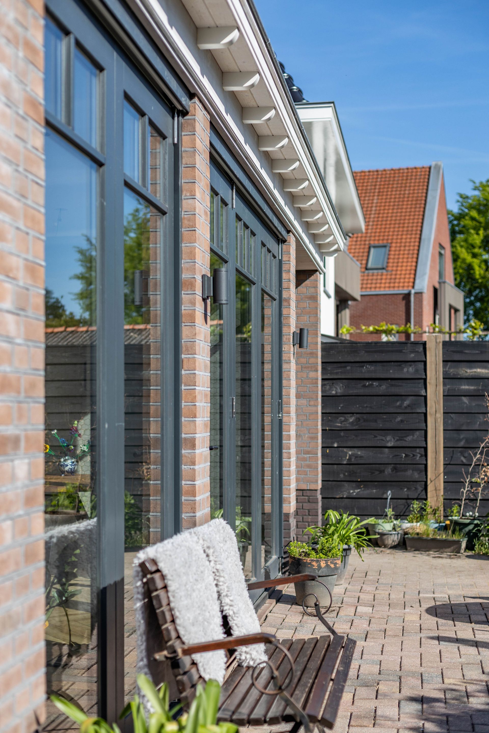 Een stenen terras naast de glazen gevel van een huis, met een houten bankje