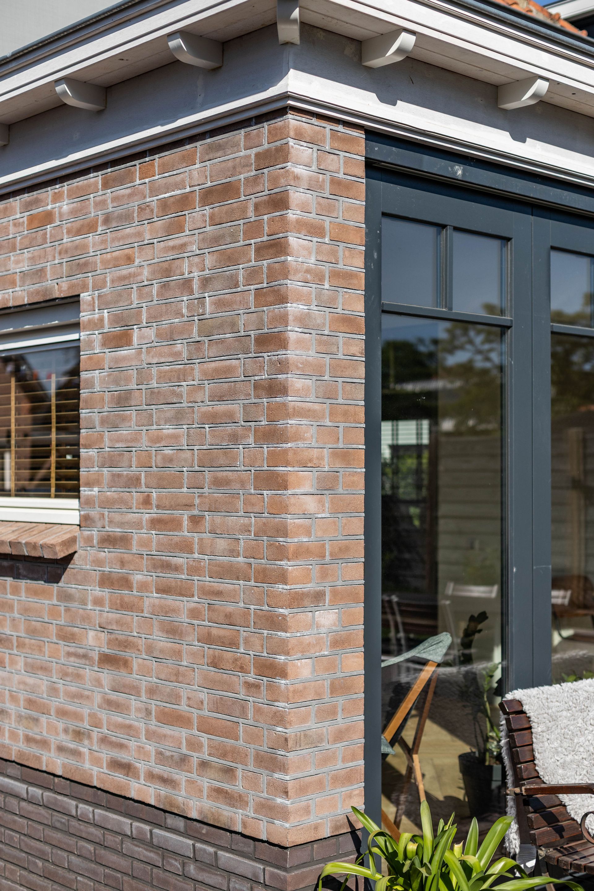 Een hoekhuis van baksteen met grote, donker omlijste glazen deuren en ramen die uitkomen op een patio.