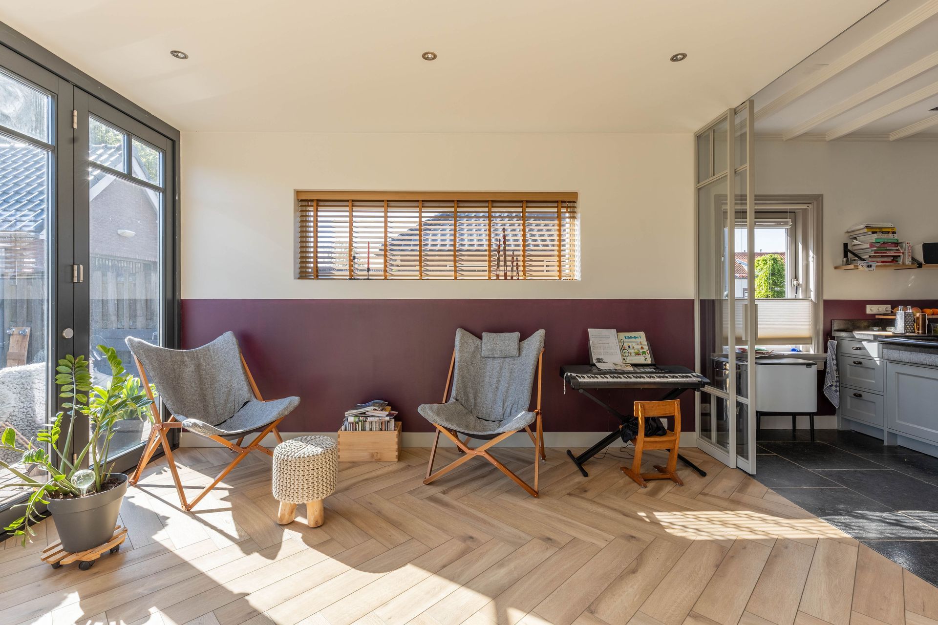 Lichte woonkamer met twee fauteuils, een tafeltje, een potplant en een open keuken met veel natuurlijk licht.