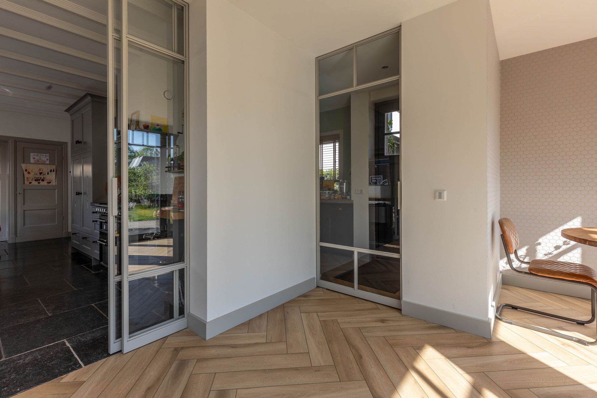 Moderne woonkamer met visgraatparketvloer, spiegeldeuren voor de kledingkast en zonlicht door een fauteuil.