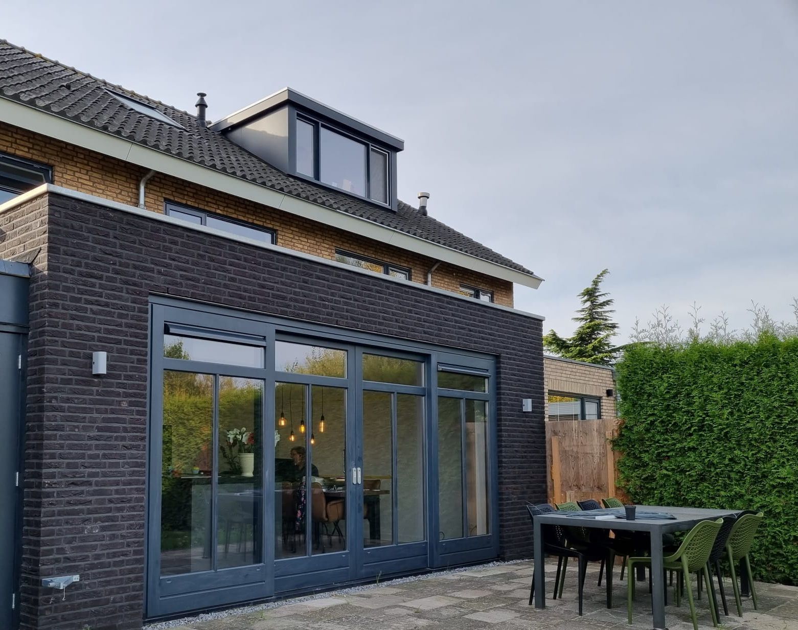 Moderne aanbouw grote ramen. Donkere schale bekleding gevel. Renovatie uitbouw.