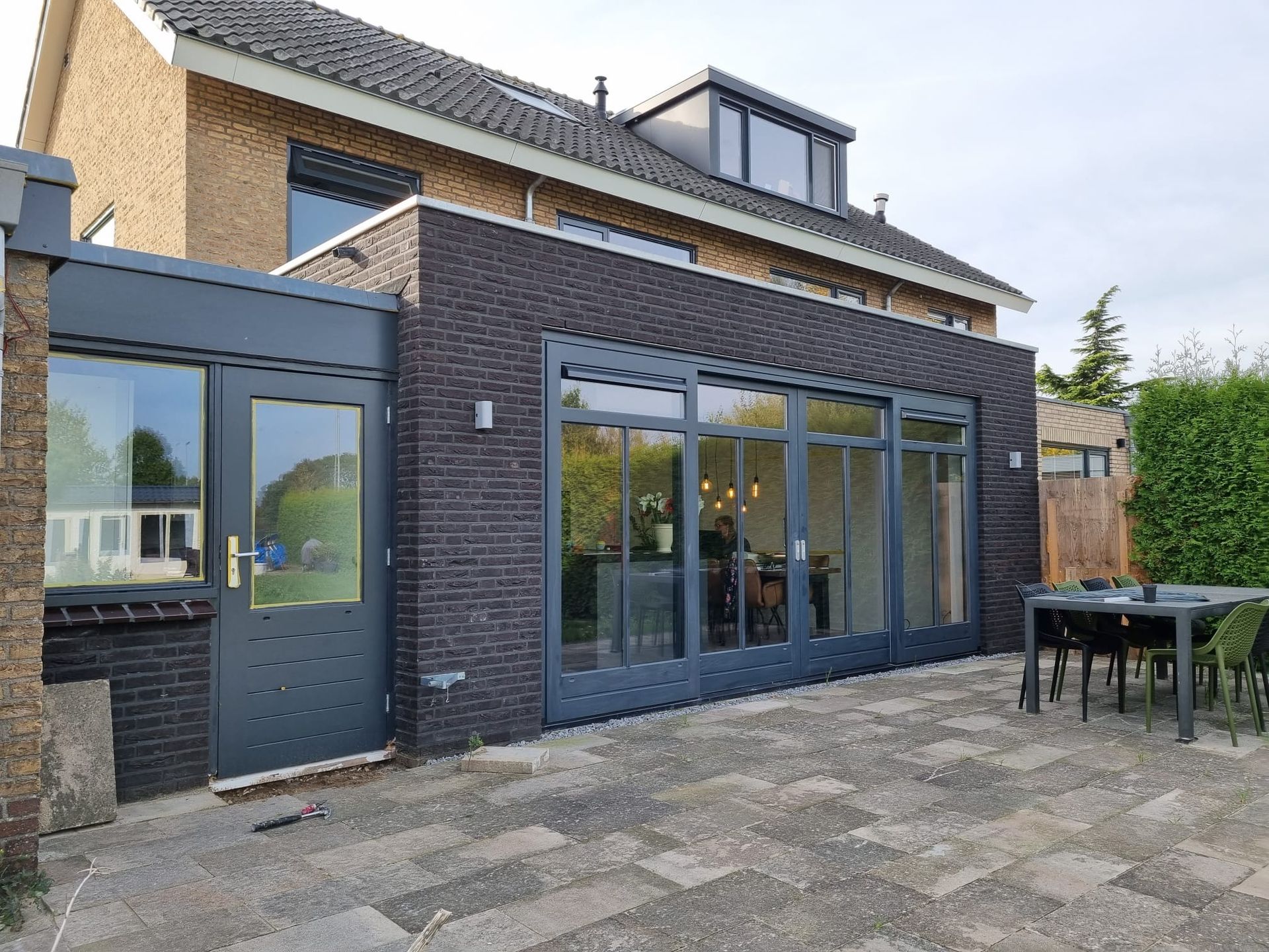 Gerenoveerde woning met moderne donkere uitbouw. Aannemer verbouwing baksteenhuis met glazen deuren.