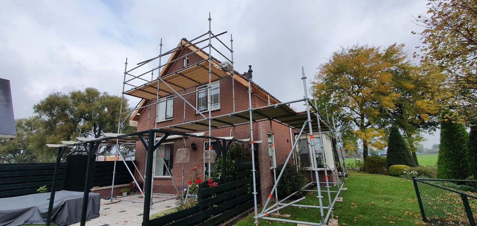 Bakstenen woning onder bouwsteiger voor gevel- en dakrenovatie. Woningrenovatie en verbouwing door aannemer.