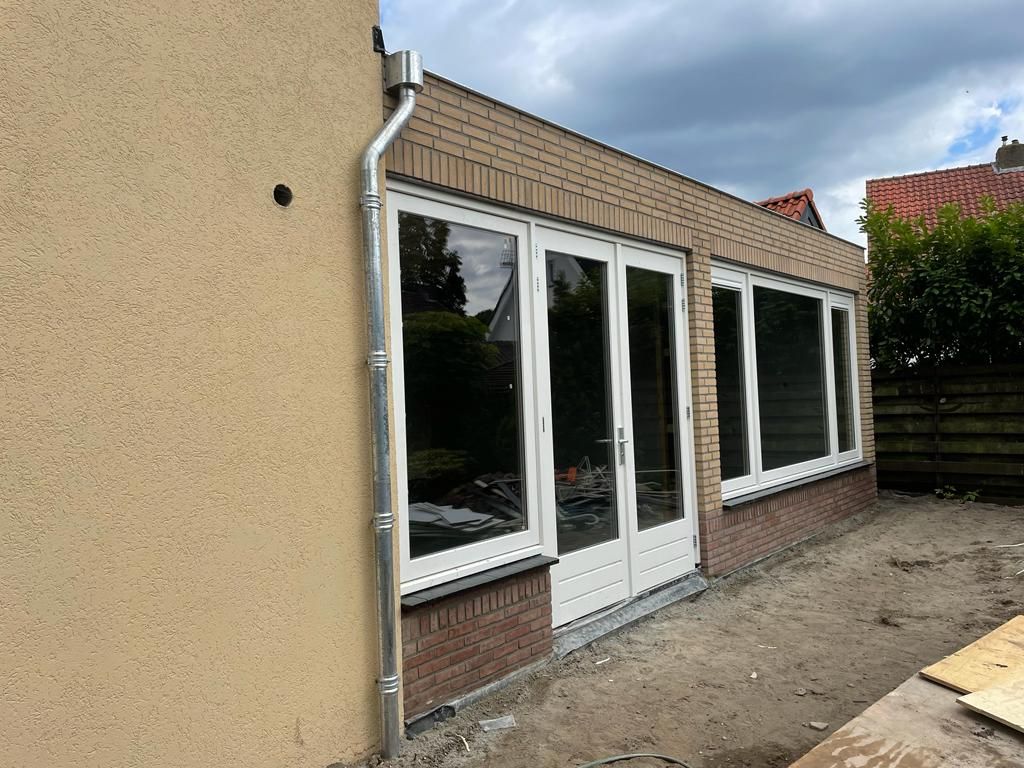 Bakstenen uitbouw met witte schuifdeuren. Aannemer verbouwing woning openslaande deuren.