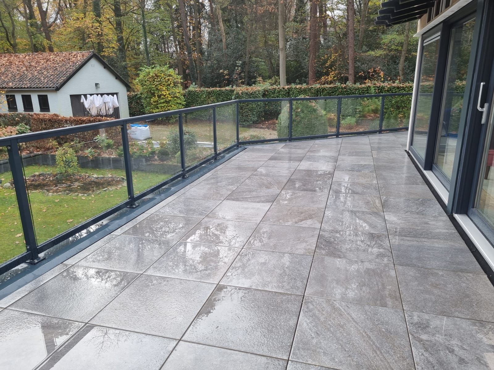 Houten terras met grijze tegels en donkere leuning. Terrasverbouwing en renovatie.