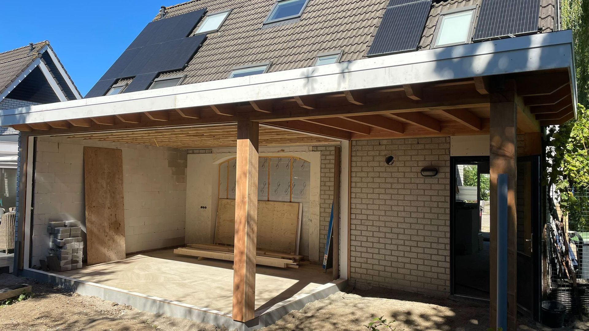 Een gedeeltelijk gebouwd huis met een houten veranda en bakstenen muren, in aanbouw.