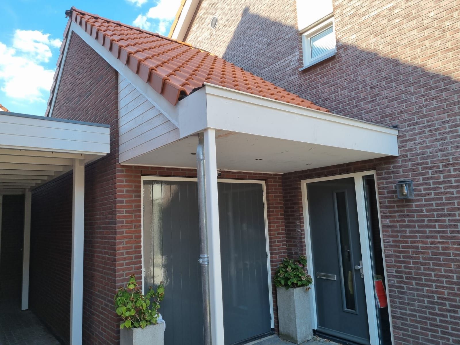 Gerenoveerde woninguitbouw met witte dak en bakstenen muur. Verbouwing aannemer moderne ramen.