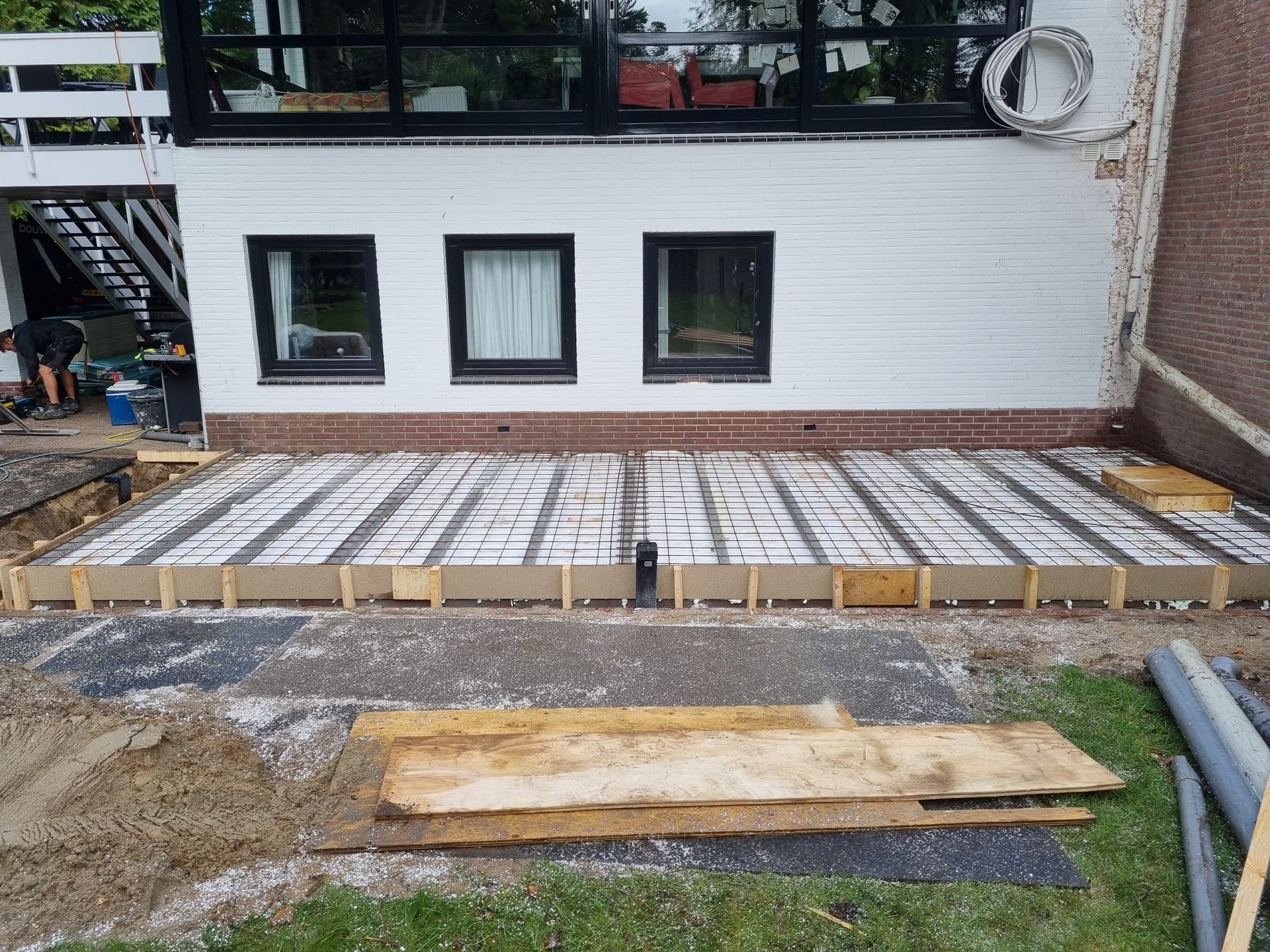 Witte aanbouw met ramen en houten terras. Verbouwing aanbouw en terrasrenovatie.
