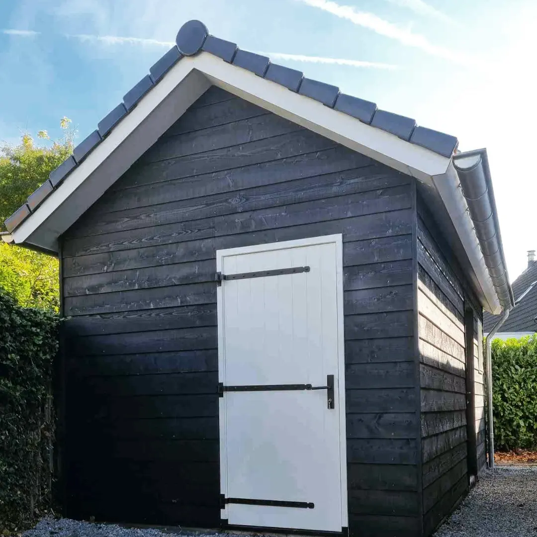 Moderne houten schuur donkere gevel. Witte deur tuinhuis verbouwing