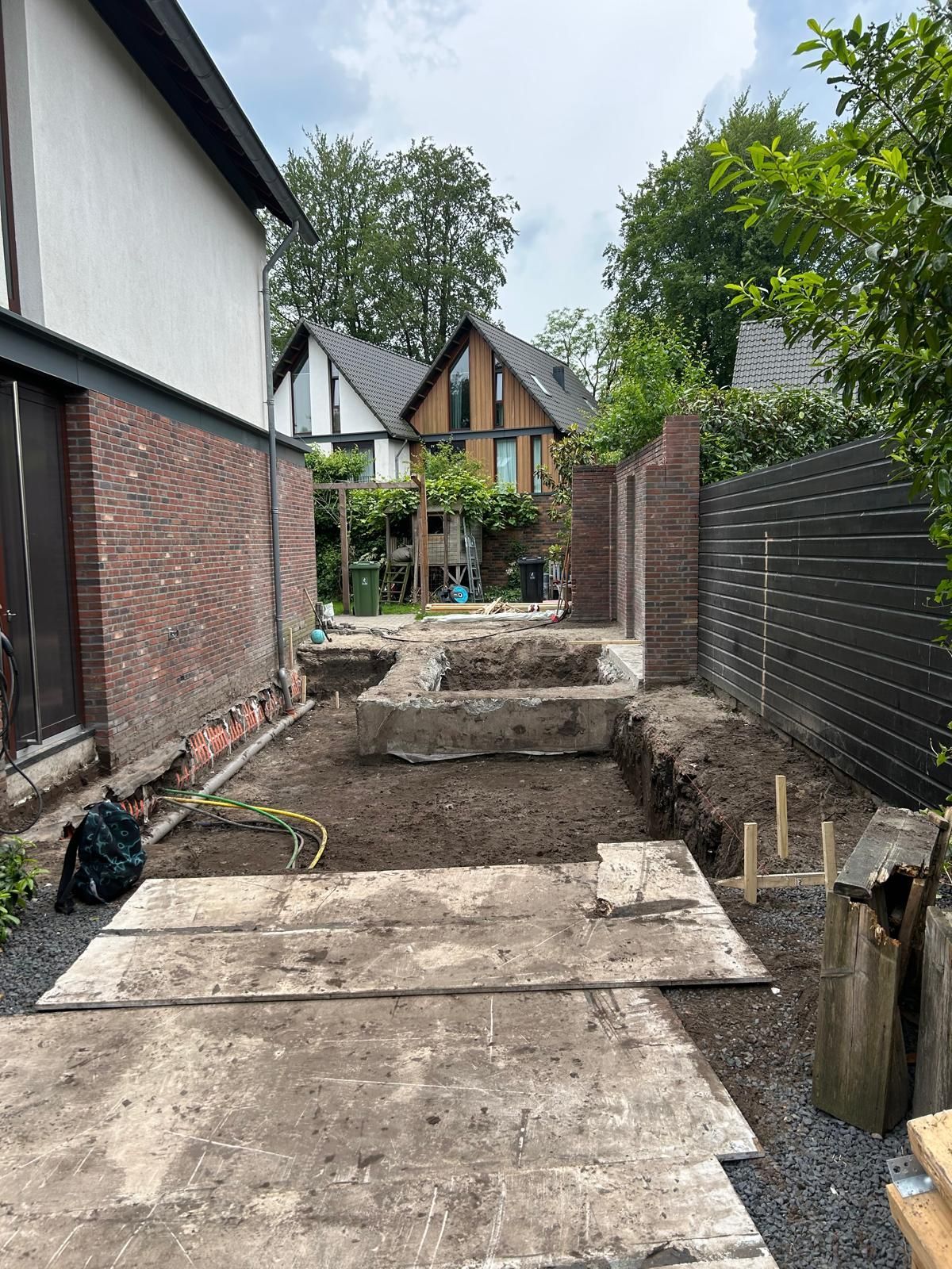 Smal tuinpad met betonnen platen, verhoogde plantenbedden en een klein huisje aan het einde.