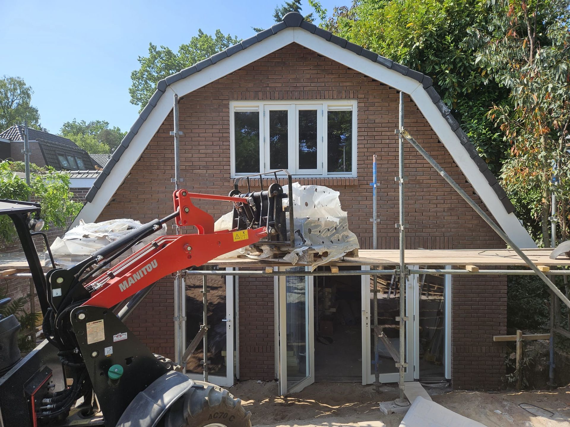 Bouwmachines slopen de voorgevel van een bakstenen huis dat wordt gerenoveerd.