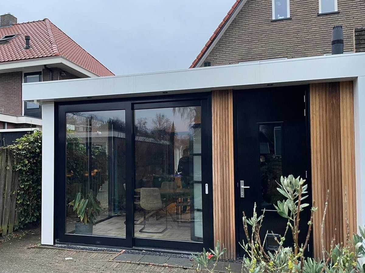 Moderne aanbouw met zwarte ramen en houten details. verbouwing woning.