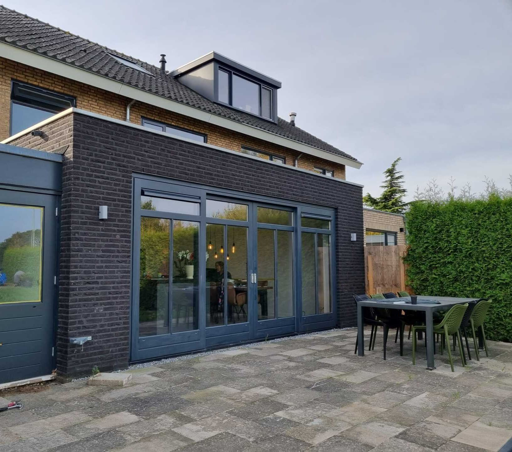 Moderne aanbouw met donkere gevel. Renovatie woning veel glas en natuurlicht.
