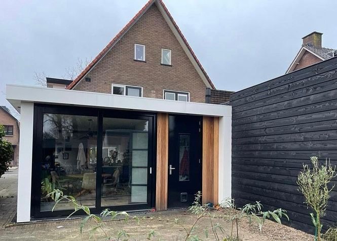 Bakstenen woning witte aanbouw houten deur. Moderne verbouwing uitbreiding.