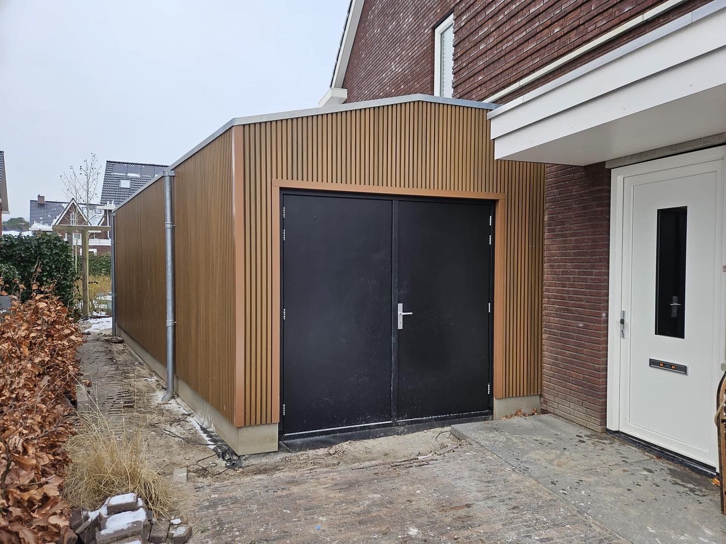 Houten aanbouw met zwarte deuren afgewerkt. Garageboxen en tuinhuisje verbouwing.