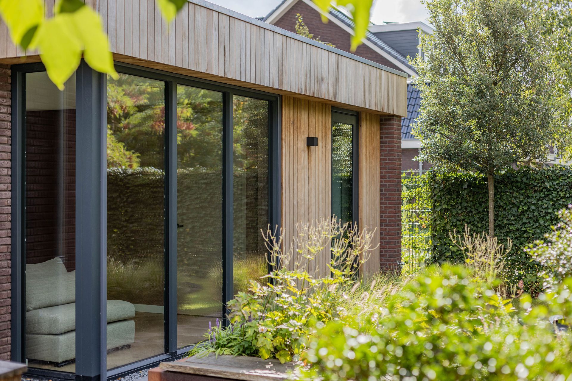 Moderne houten uitbouw met schuifdeuren. Grote ramen en terras. Woonuitbreiding glas