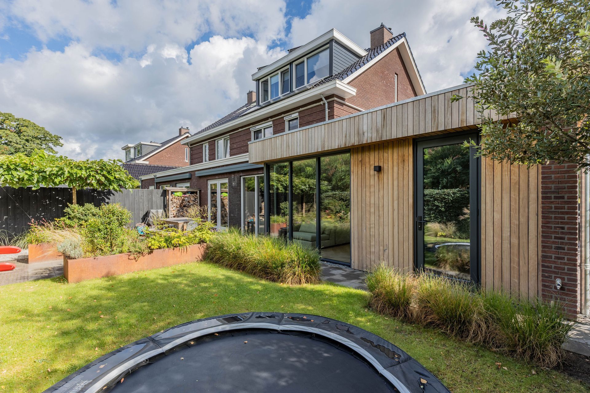 Gerenoveerde achtergevel bakstenen woning met houten aanbouw.