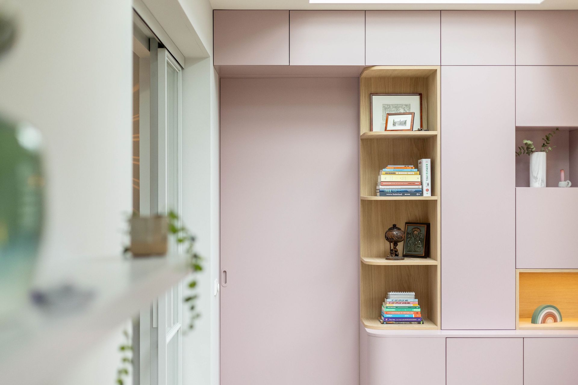 Moderne kamer met ingebouwde planken, boeken, decoratie en een groot raam aan de linkerkant.