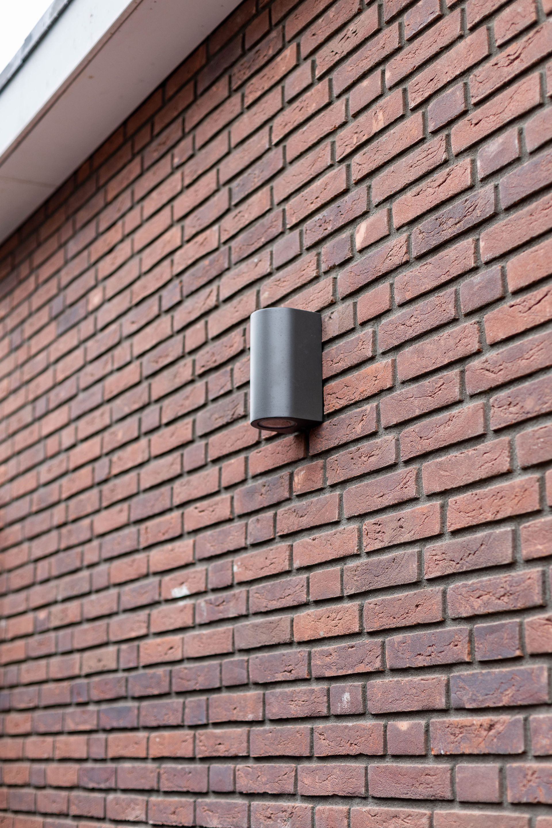 Grijze wandlamp aan een rode bakstenen buitenmuur.